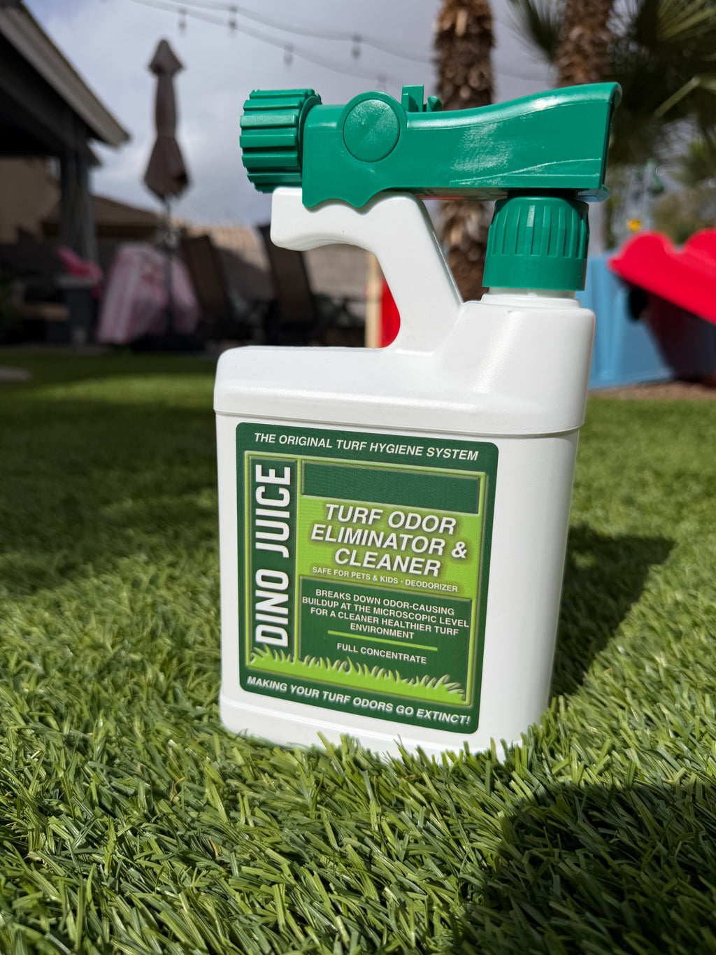 Spray bottle labeled 'Dino Juice turf odor eliminator and cleaner' on artificial grass