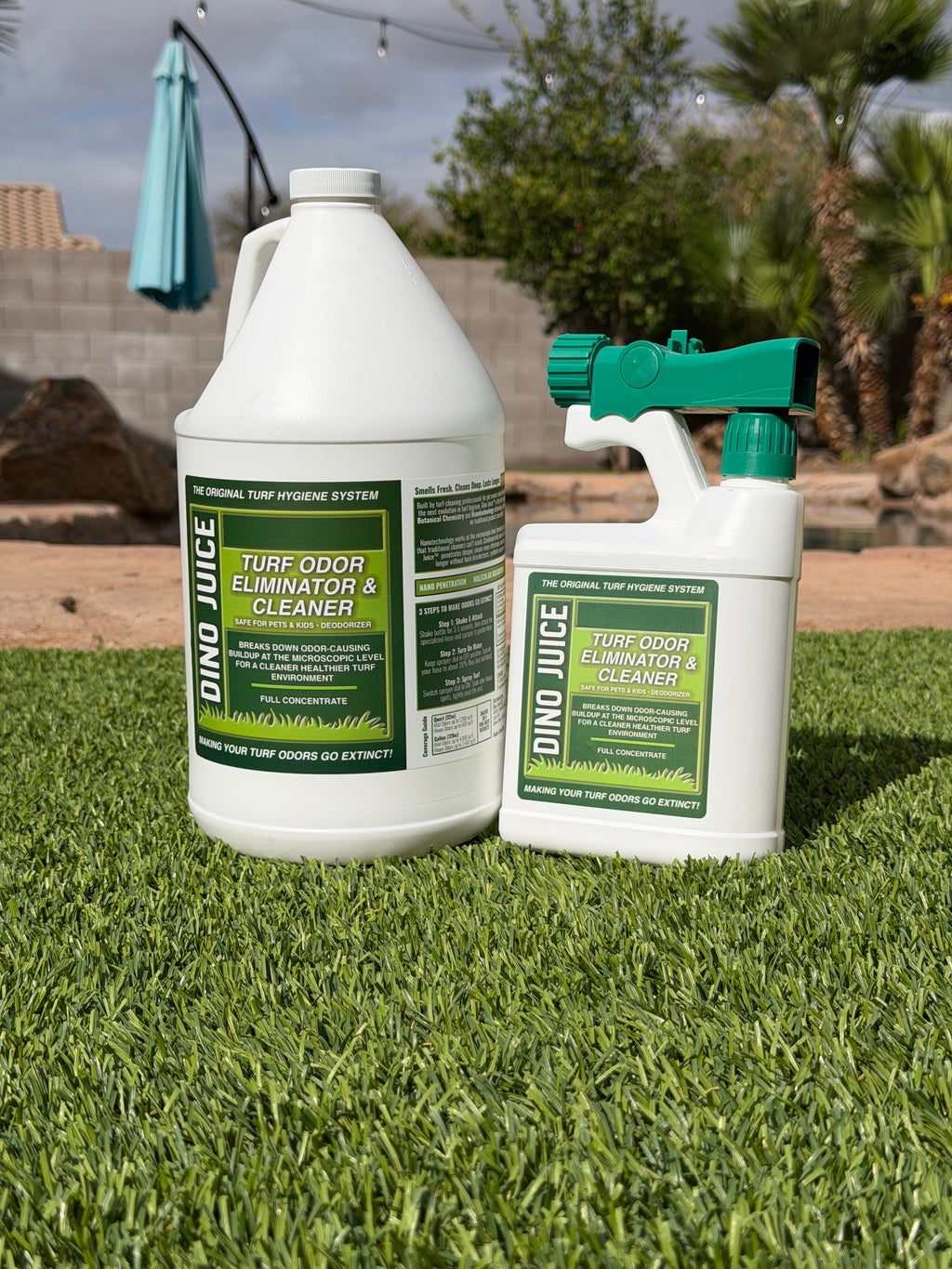 Two bottles of 'Dino Juice' turf odor eliminator and cleaner on grass with a blurred background